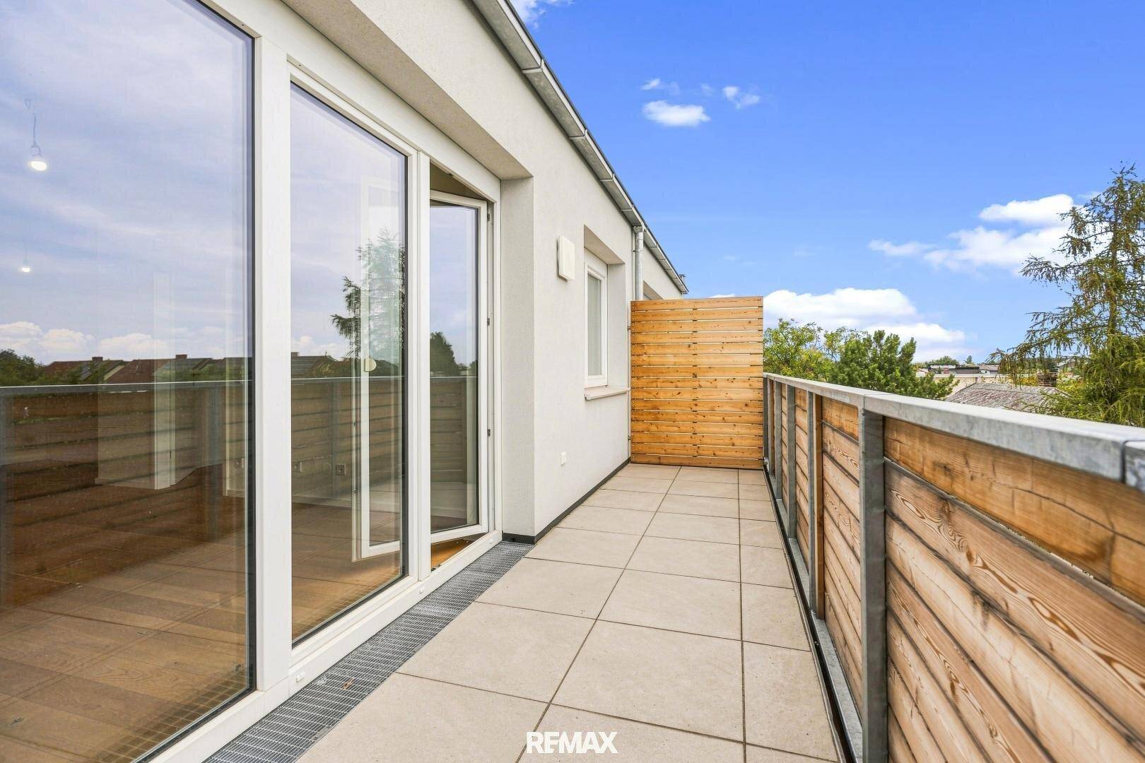 Langer Balkon mit Fliesenboden und Holzverkleidung, zugänglich durch große Glastüren, ideal zum Entspannen.