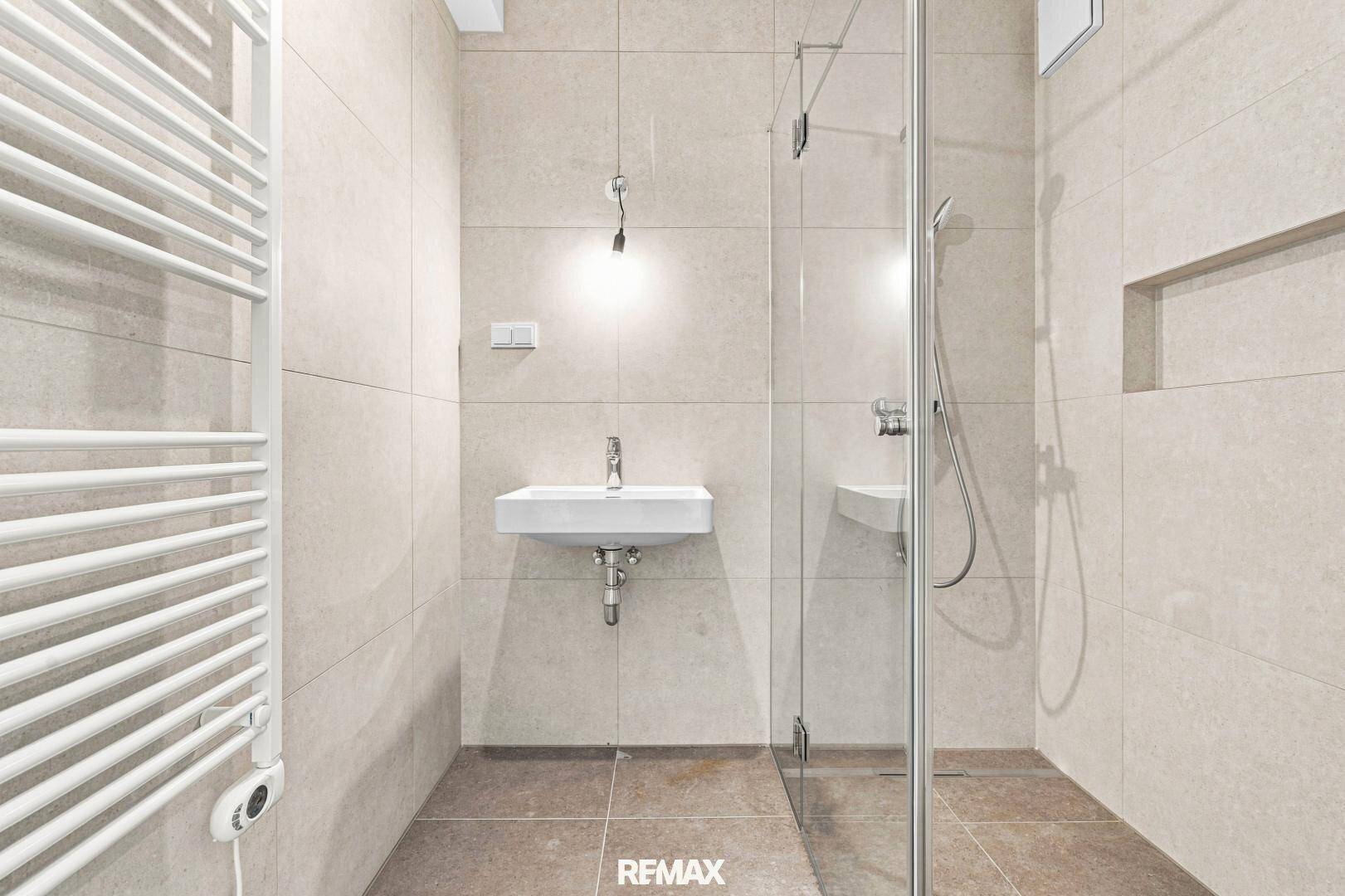 Helles Badezimmer mit Duschkabine, Waschbecken und beheiztem Handtuchhalter, bietet Komfort und modernes Design.