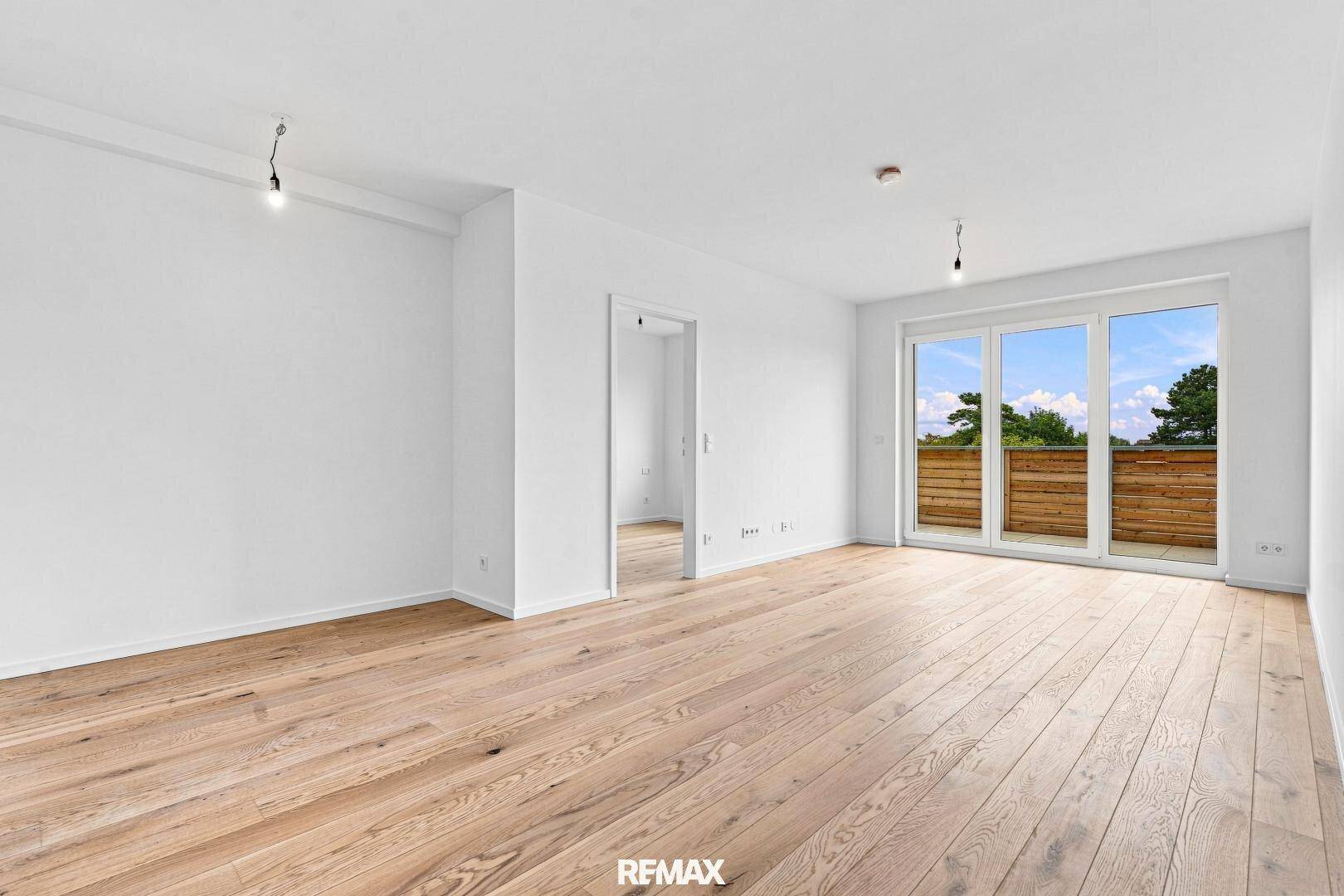 Heller Wohnbereich mit Holzboden und großen Fenstern, die auf einen Balkon führen und viel Licht spenden.