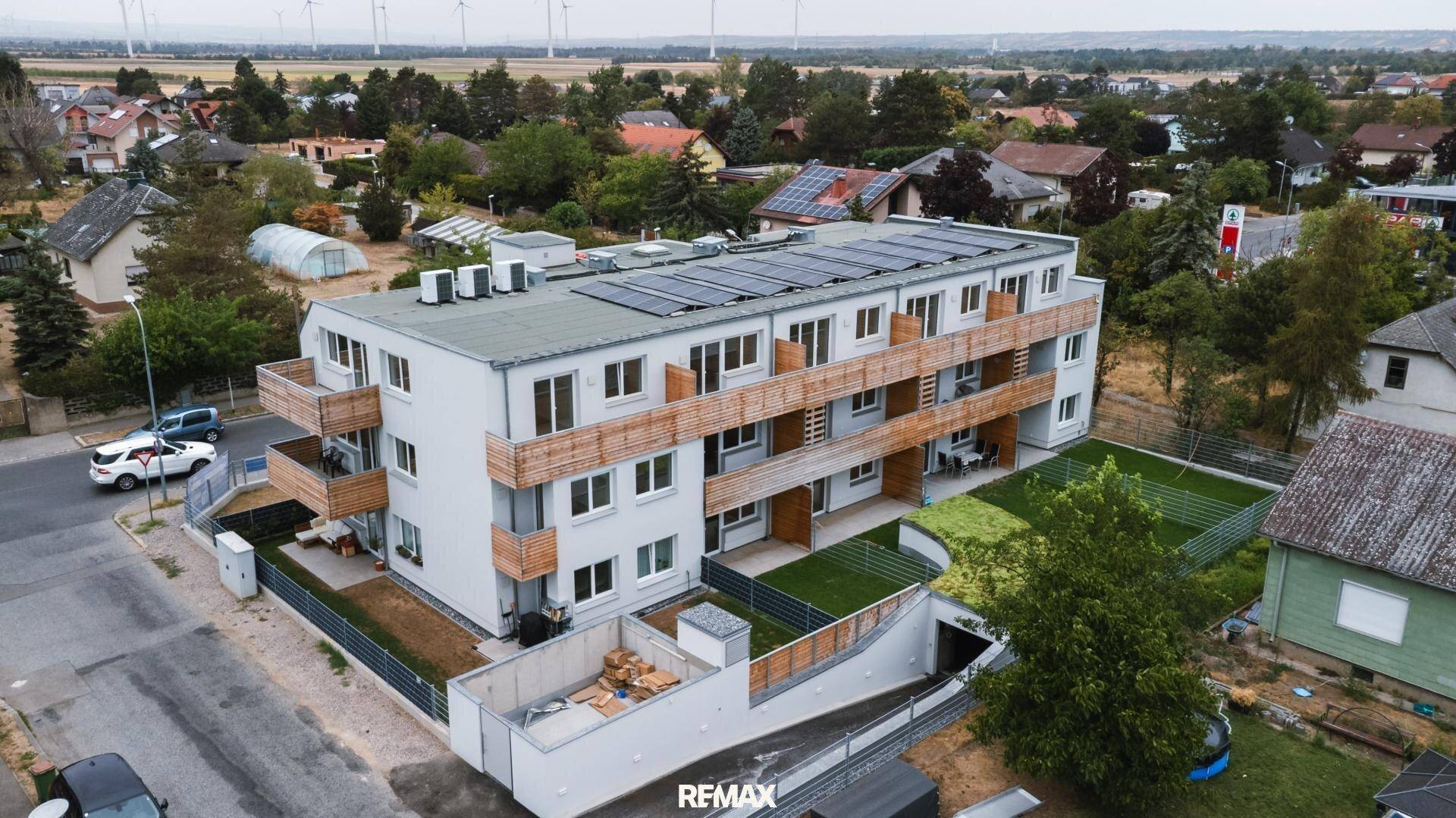 Luftaufnahme eines modernen Wohngebäudes mit Balkonen, Grünflächen und Solaranlage auf dem Dach.