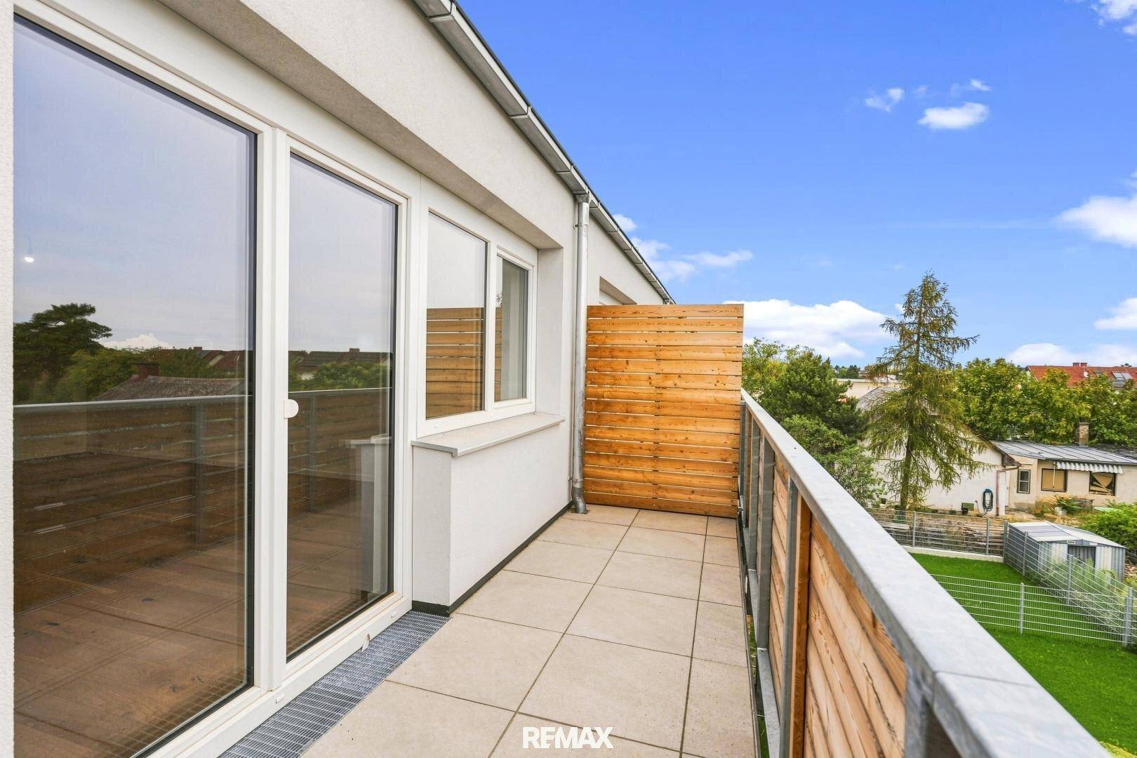 Heller Balkon mit Fliesenboden und Holzverkleidung, bietet viel Tageslicht durch große Fenster.