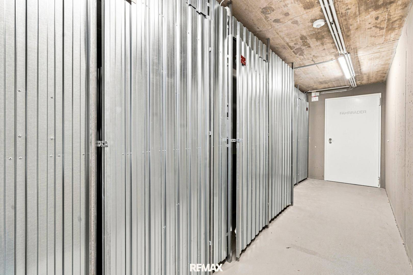 Reihe von Metall-Abstellboxen in einem Kellerraum mit Betonwänden und -decke.