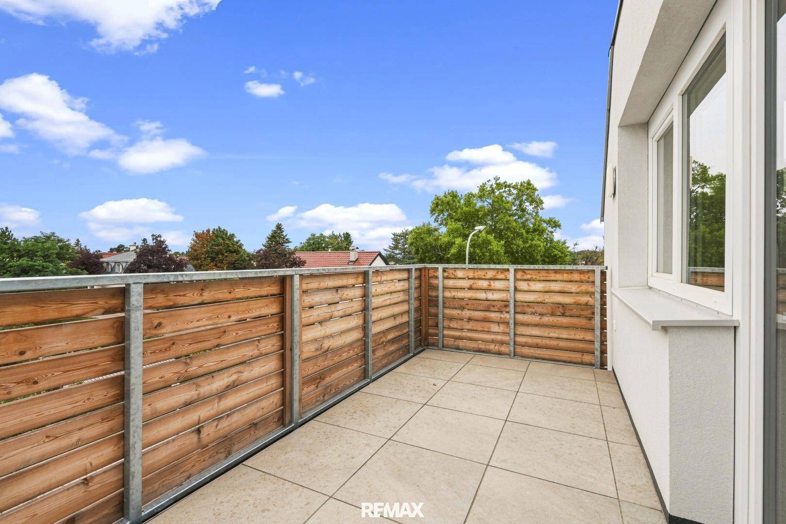 Geräumige Terrasse mit Holzsichtschutz und weitem Blick in die grüne Umgebung unter blauem Himmel.