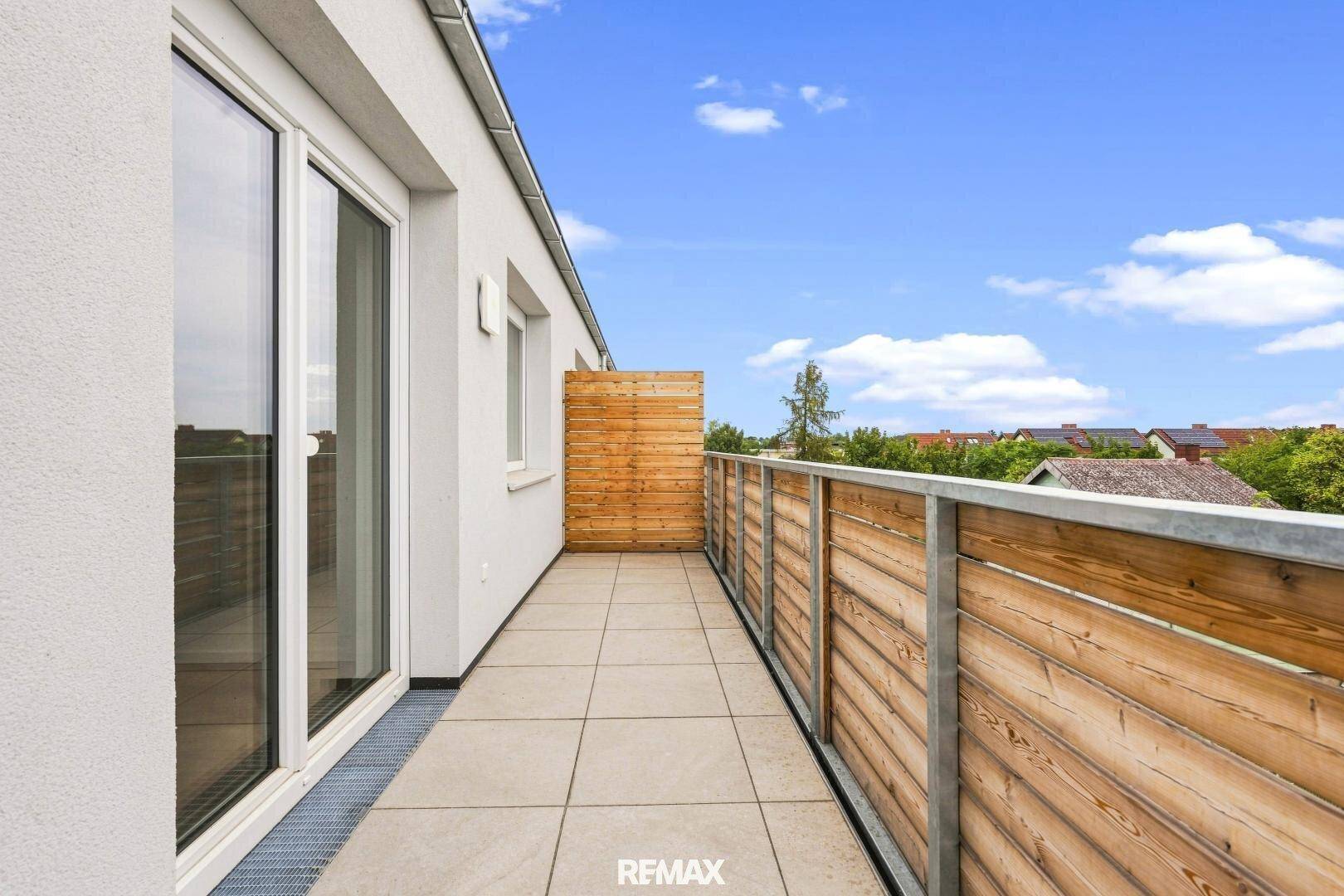 Heller Terrassenbereich entlang der Fassade mit Zugang zu den Innenräumen und viel Tageslicht.