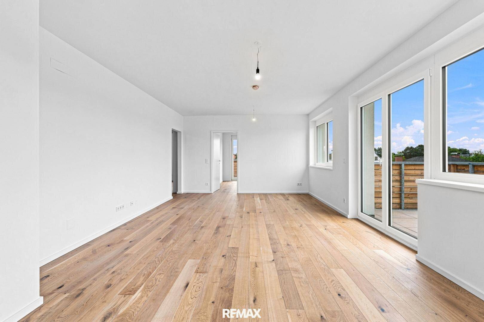 Heller Wohnbereich mit Holzboden, Zugang zur Terrasse und offener Tür zu weiteren Zimmern der Wohnung.