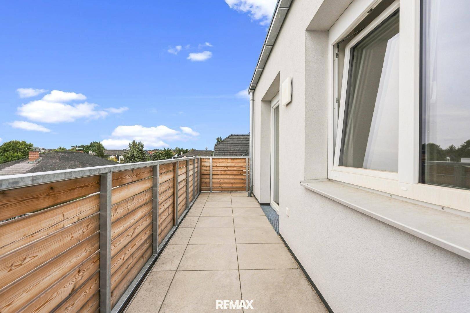 Lange, sonnige Terrasse mit Fliesenboden und Holzsichtschutz, ideal zum Entspannen im Freien.
