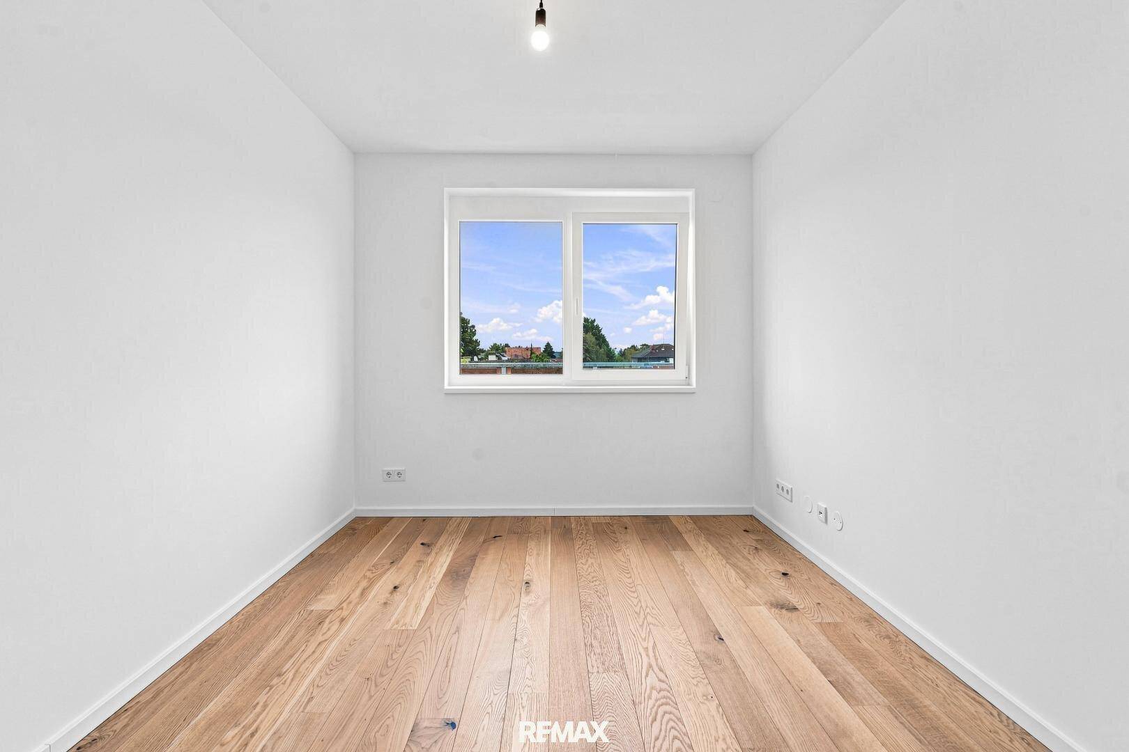 Ruhiges, helles Zimmer mit Holzboden und einem Fenster, das einen Blick ins Grüne bietet.