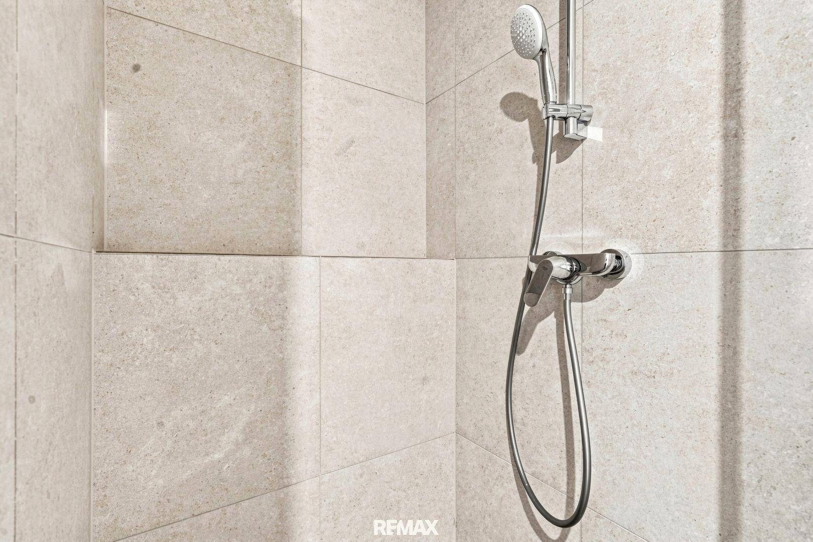 Detailaufnahme einer modernen Dusche mit beigefarbenen Fliesen und einer praktischen Handbrause.