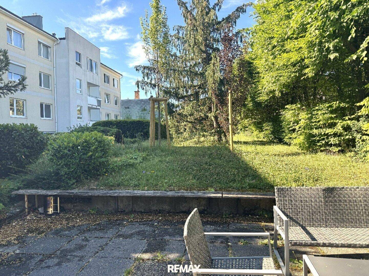 Gemeinschaftsgarten mit Sitzgelegenheiten und viel Grünfläche hinter dem Gebäude, ideal zur Entspannung.