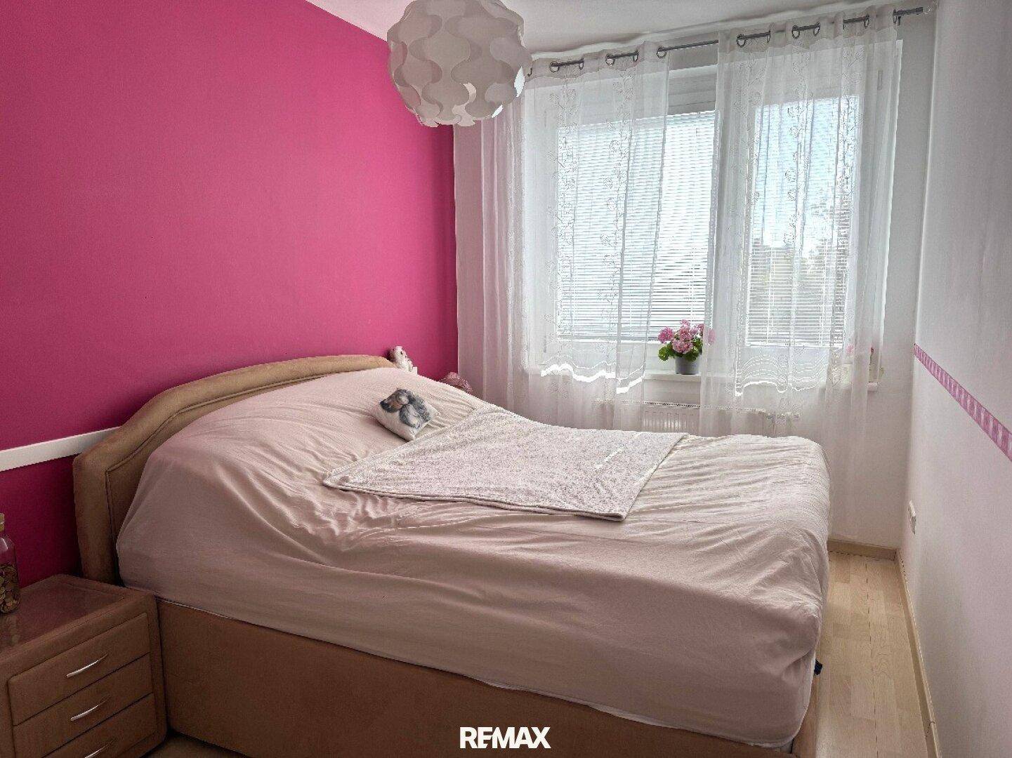 Schlafzimmer mit rosa Wänden, Doppelbett und großem Fenster für viel Tageslicht.
