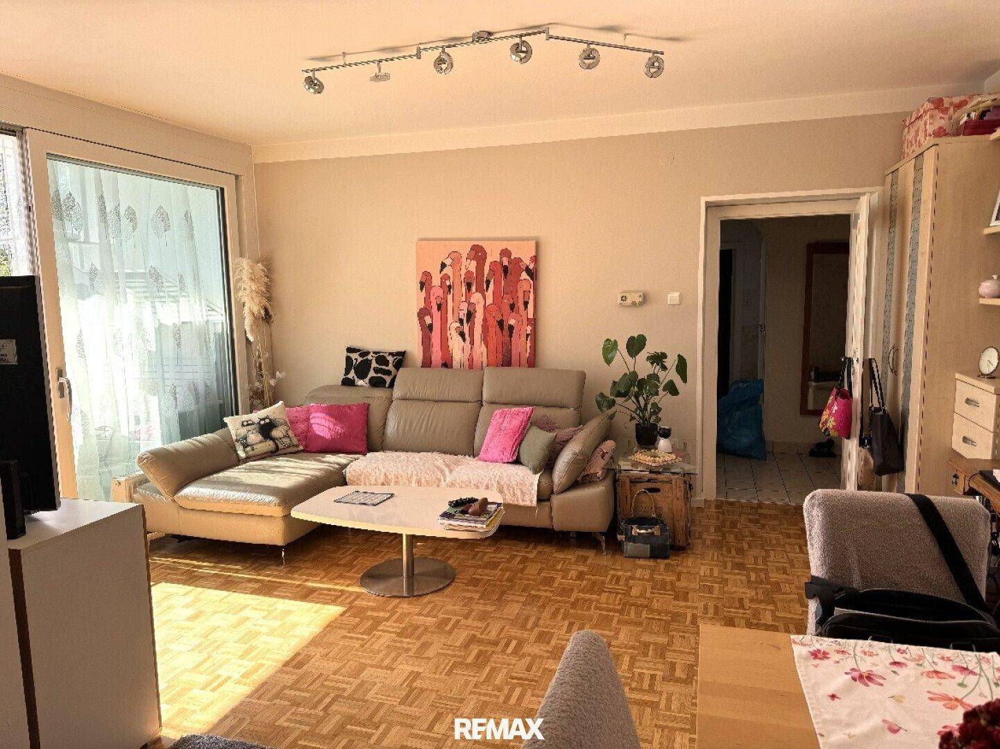 Geräumiges Wohnzimmer mit Parkettboden, Sofa und Blick auf den Balkon, hell und einladend.