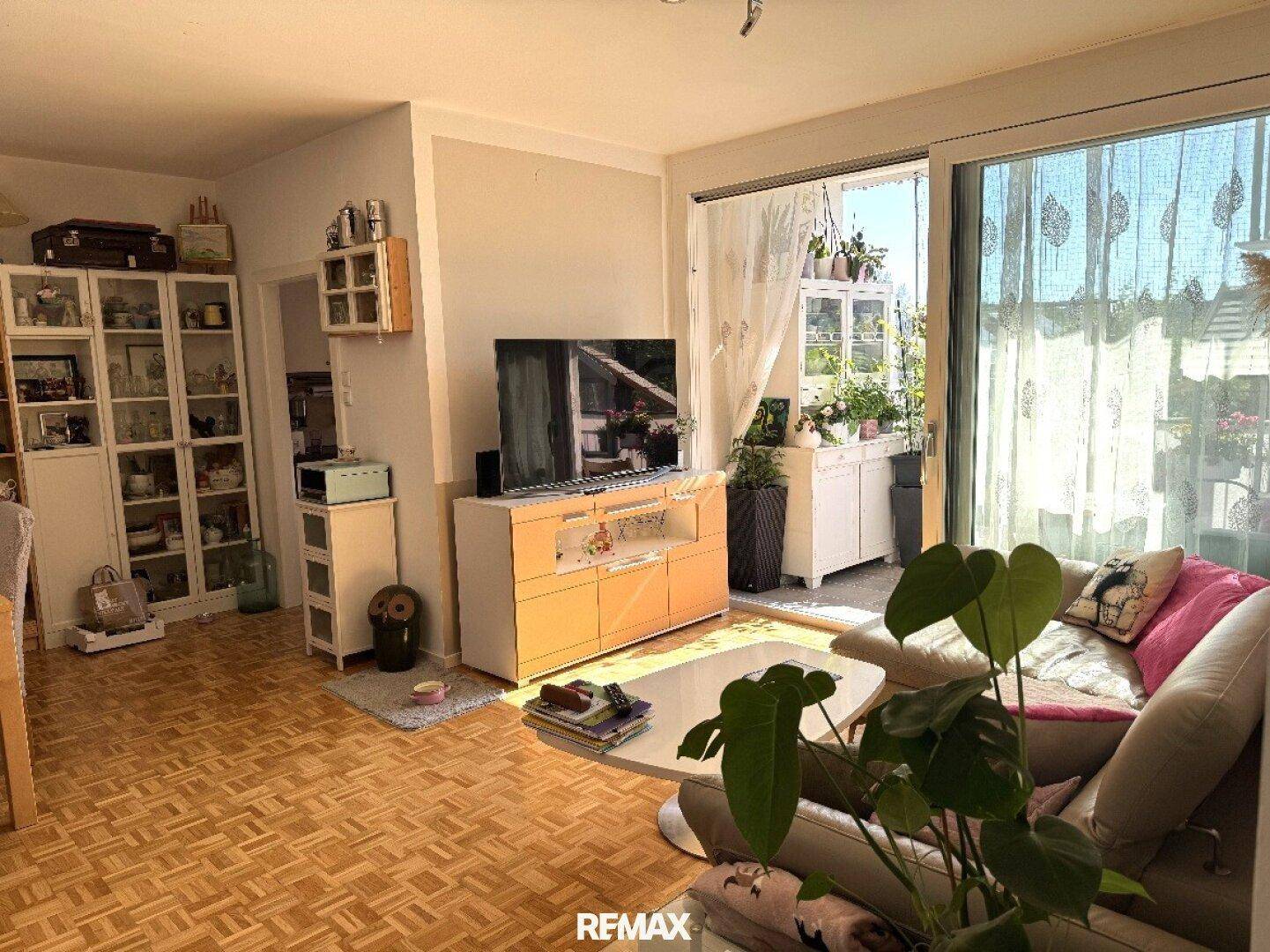 Helles Wohnzimmer mit Sofa, TV-Möbel und Zugang zum sonnigen Balkon, modern eingerichtet.