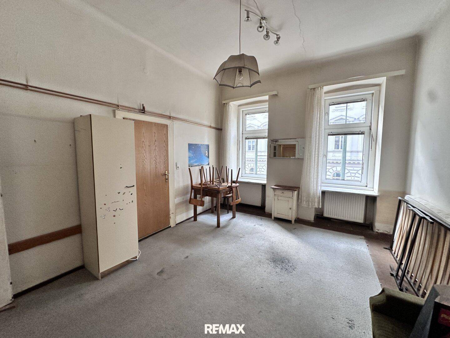 Helles Schlafzimmer mit Teppichboden, Schrank und zwei Fenstern, die viel Licht hereinlassen.