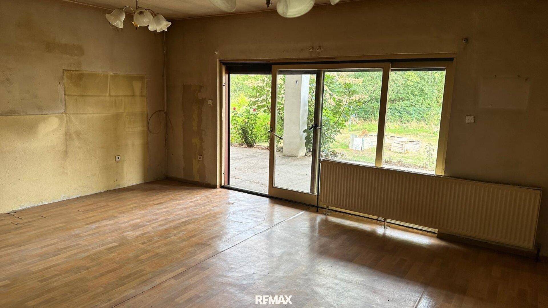 Leeres Wohnzimmer mit Holzboden und Zugang zu einer Terrasse oder Garten.