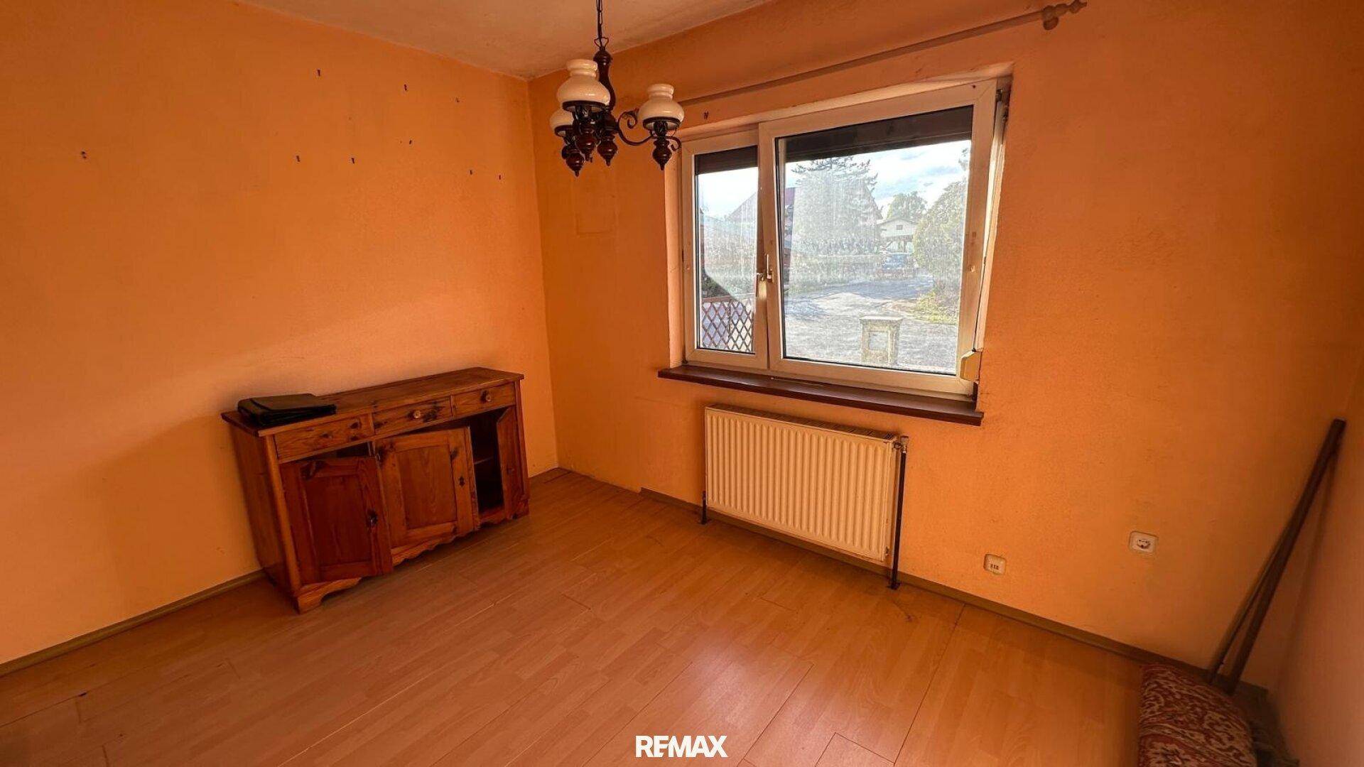 Leeres Zimmer mit Laminatboden, Fenster und einem alten Holzschrank.