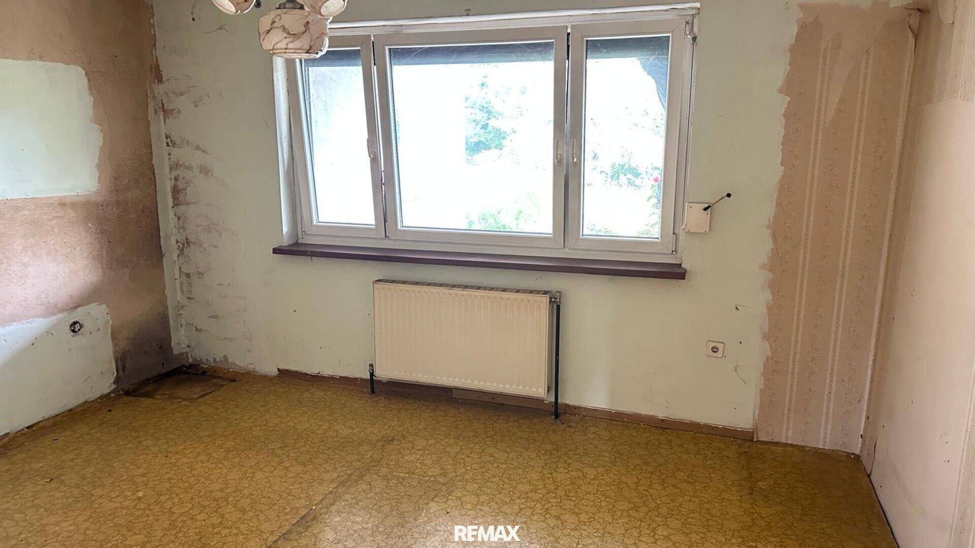 Leeres Zimmer mit abgenutztem Bodenbelag und Fenster, bereit für Renovierung.