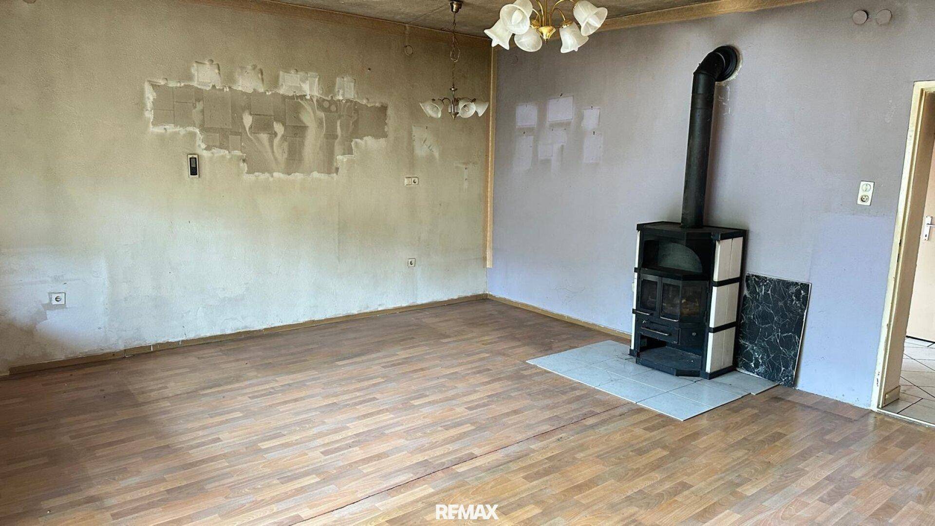 Geräumiges Wohnzimmer mit einem Holzofen und abgenutztem Parkettboden.