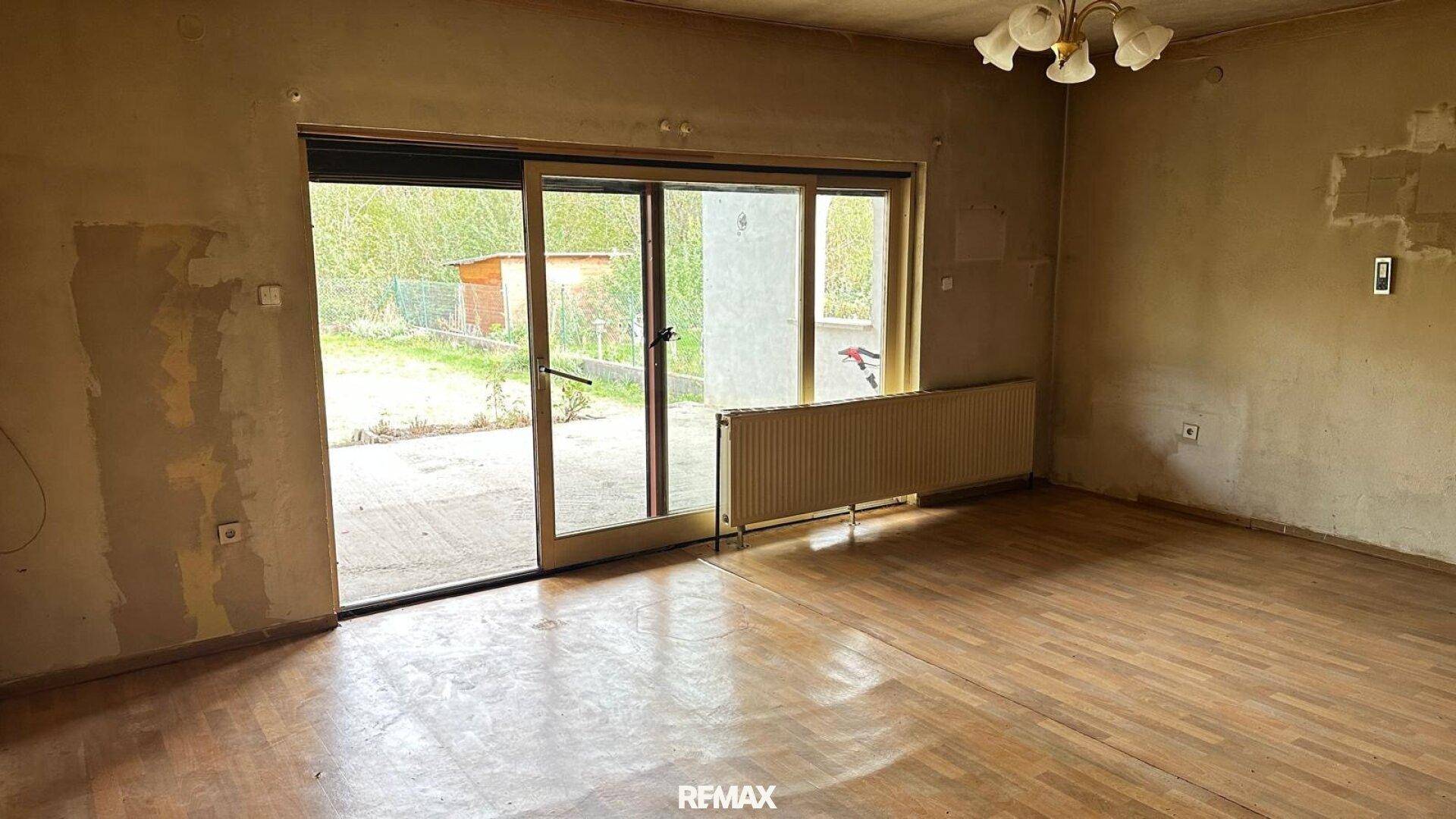 Leeres Wohnzimmer mit Holzboden und Schiebetür zum Gartenbereich.