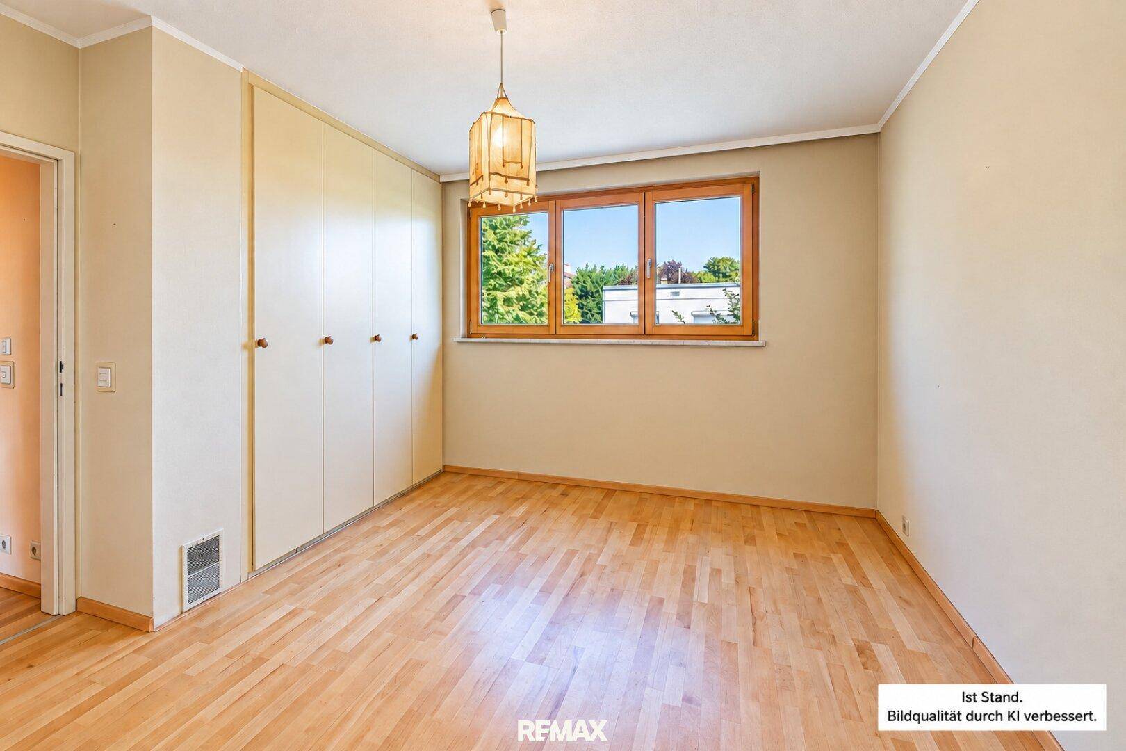 Helles Schlafzimmer mit Holzfußboden, Einbauschränken und großem Fenster.