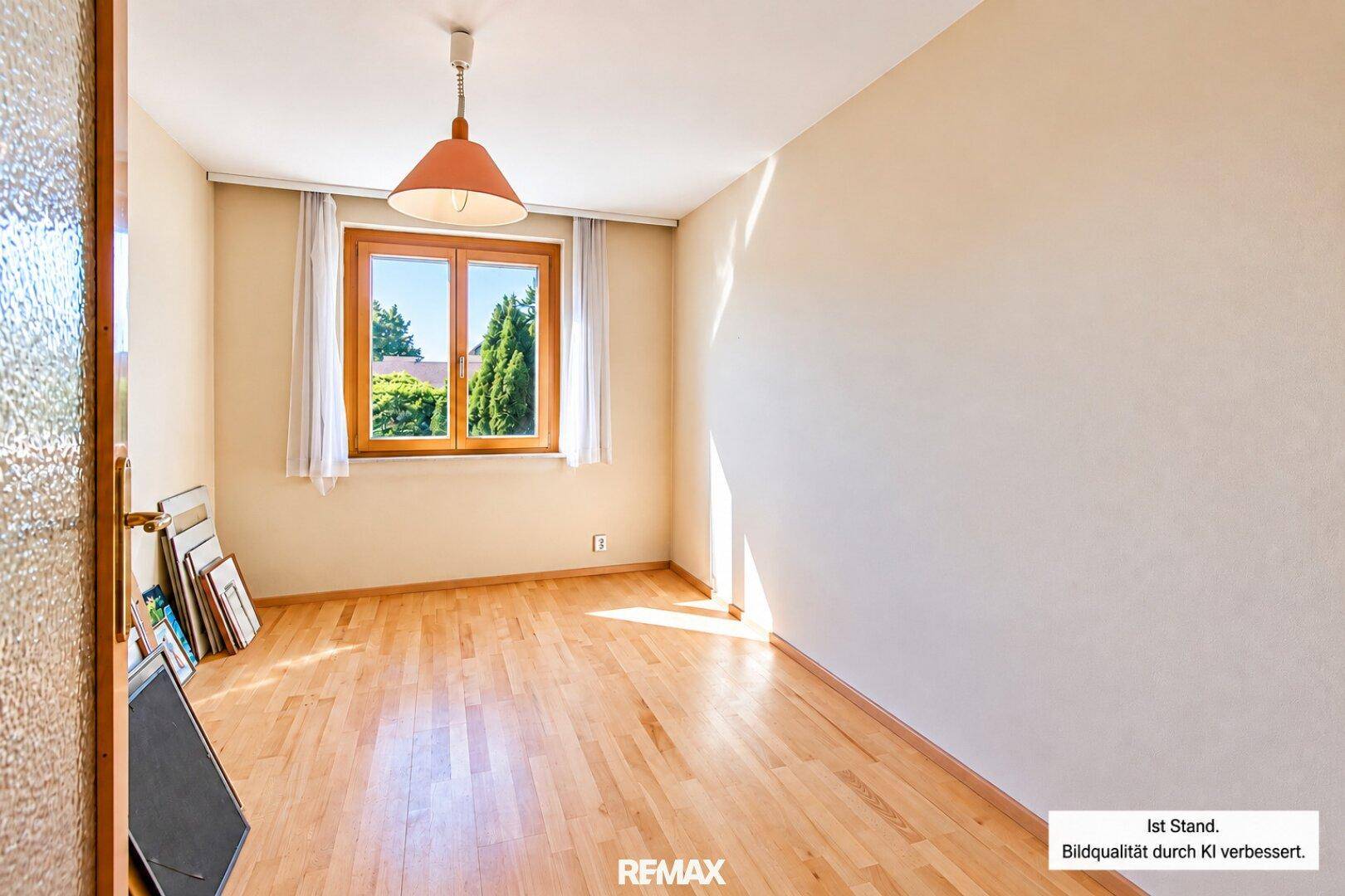 Helles Zimmer mit Holzfußboden und großem Fenster, ideal als Arbeits- oder Gästezimmer.