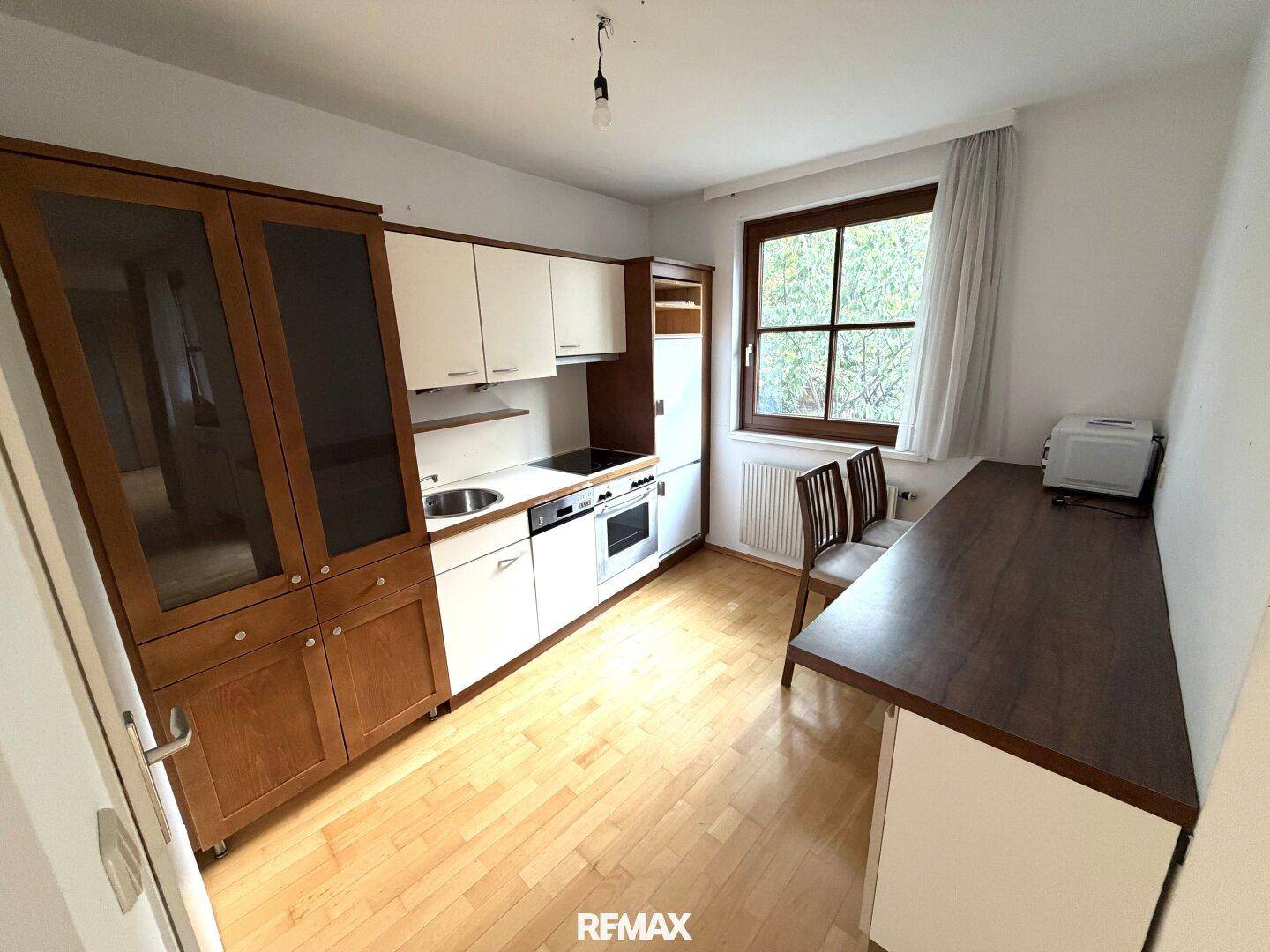 Funktionale Küche mit Holz- und weißen Schränken, Fenster und integriertem Essbereich.