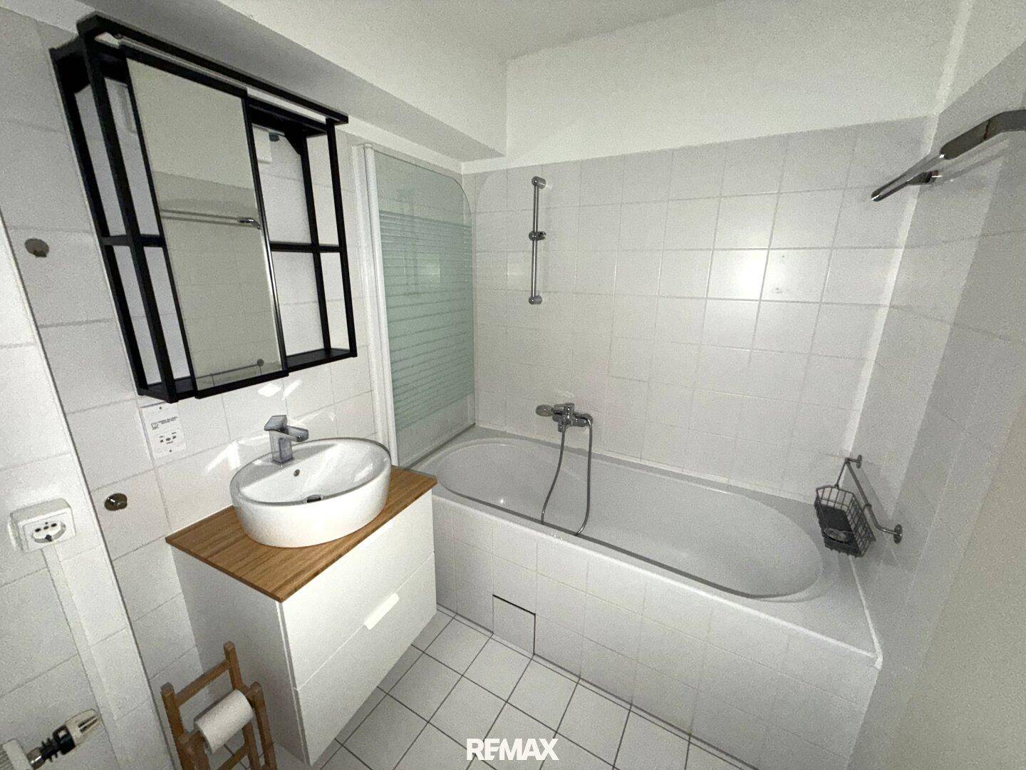 Modern gefliestes Badezimmer mit Badewanne, Dusche und Waschbecken mit Unterschrank.