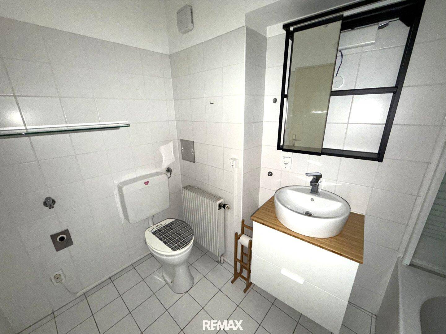 Helles Badezimmer mit WC, Waschbecken und Spiegel, komplett gefliest in Weiß.