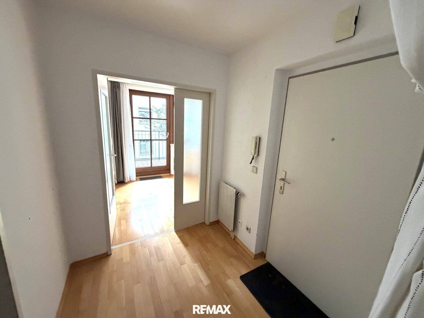 Heller Flur mit Parkettboden und Zugang zum Wohnbereich mit Balkon.