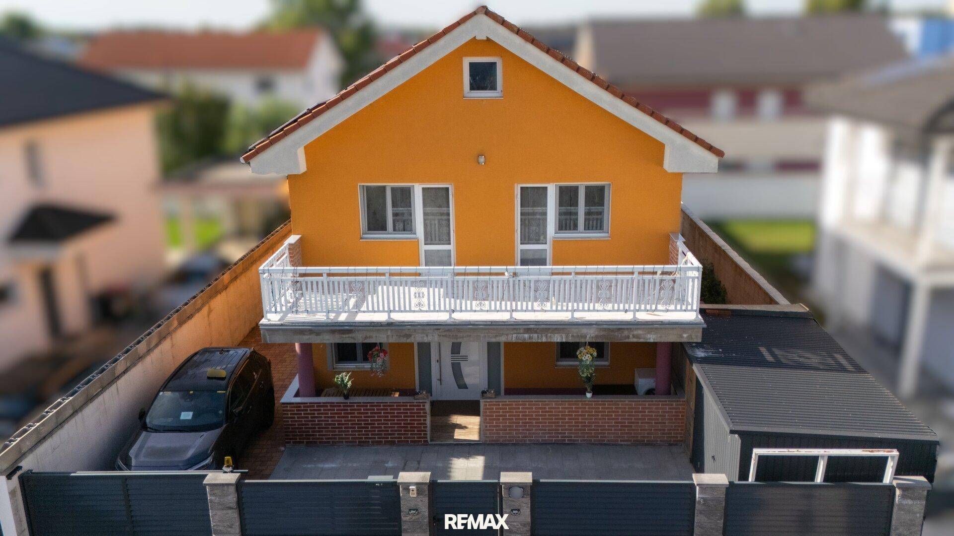 Vorderansicht des Einfamilienhauses mit gelber Fassade, weißem Balkongeländer und Eingangsbereich.