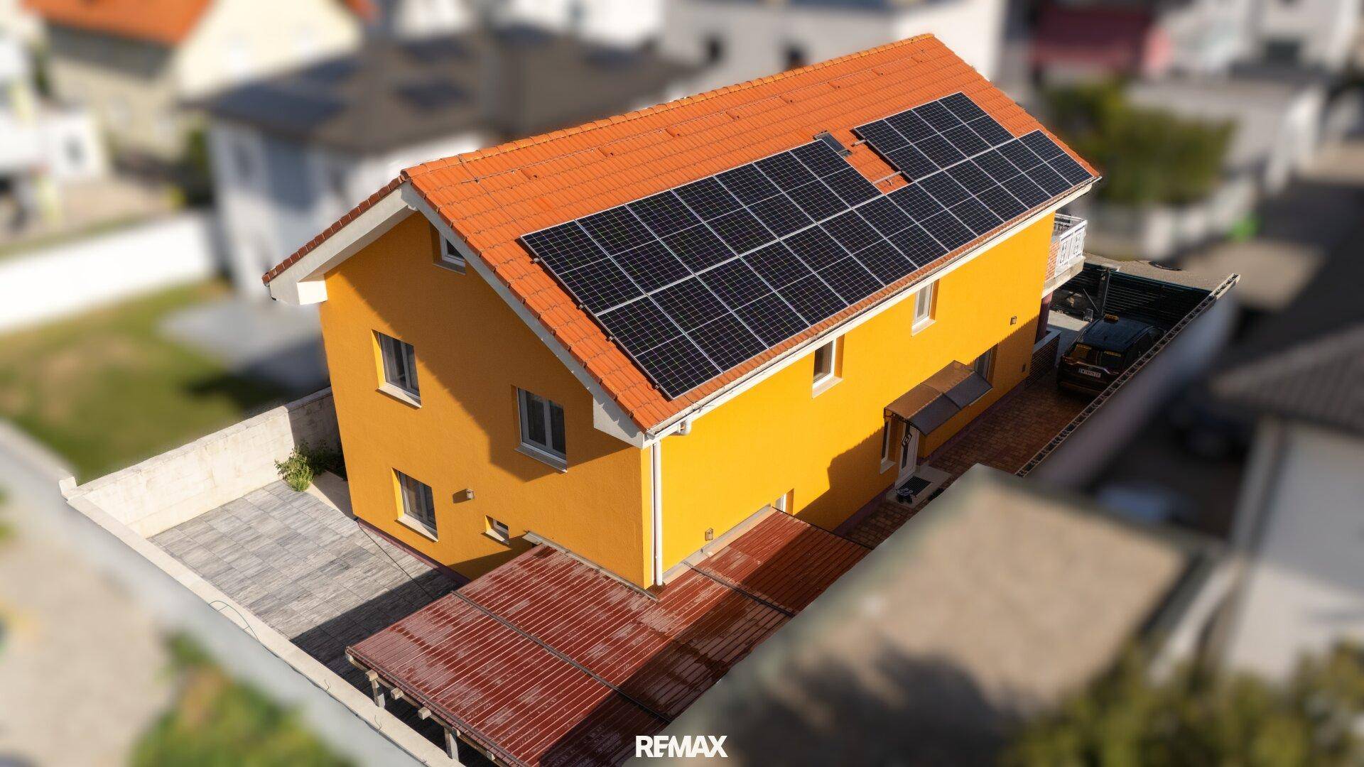 Luftaufnahme des Hauses mit Solaranlage auf dem Dach, gelber Fassade und einem Balkon.