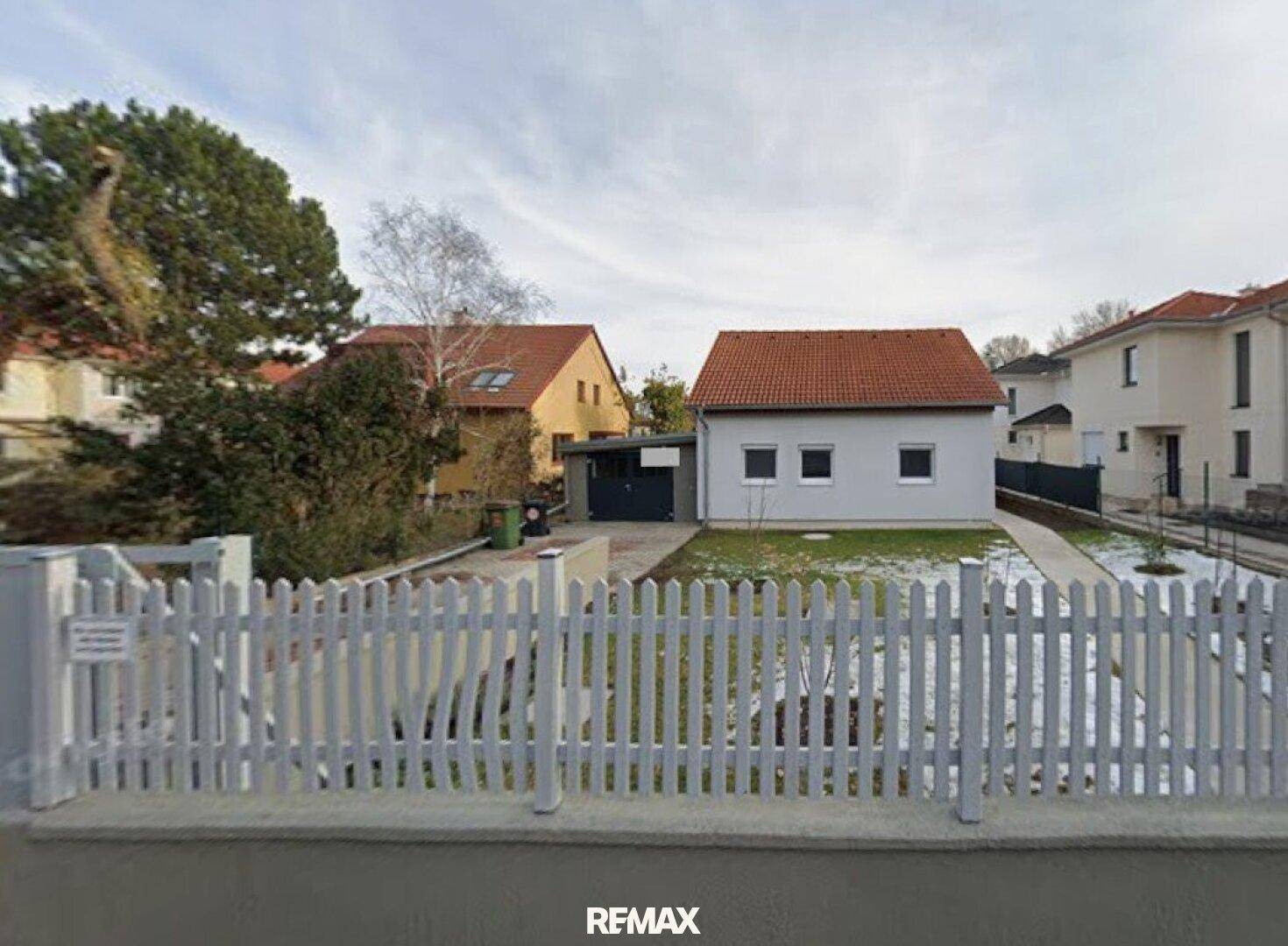 Vorderansicht eines Hauses mit weißem Lattenzaun, kleinem Vorgarten und angrenzender Garage.