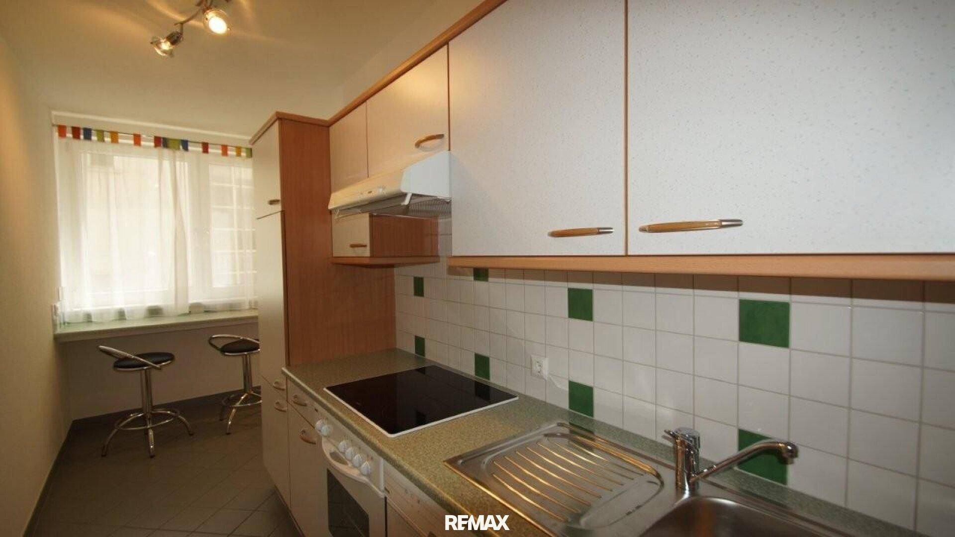 Funktionale Küche mit weißen Schränken, Fliesenrückwand und einem kleinen Essbereich am Fenster.