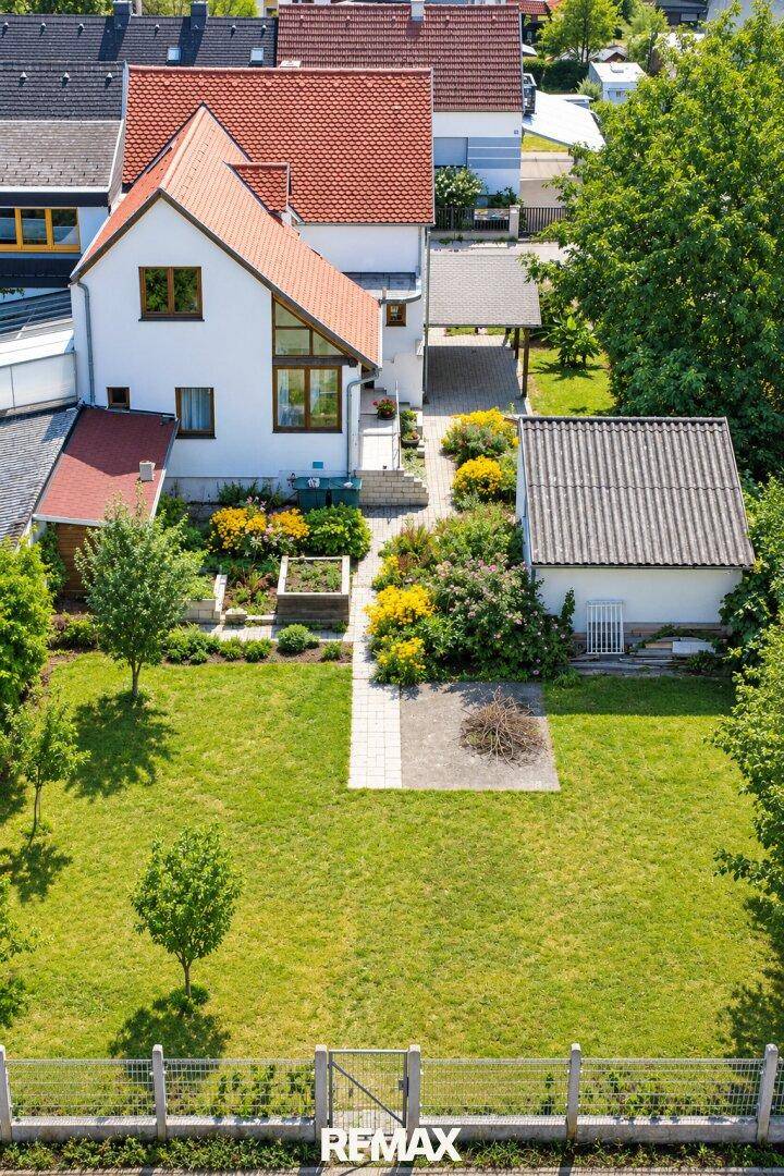 Vogelperspektive eines Einfamilienhauses mit großem Rasenbereich und angelegten Blumenbeeten im Garten.