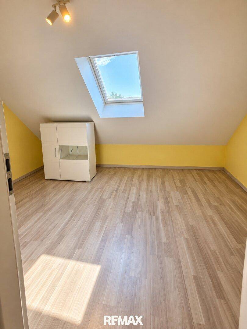 Helles Zimmer im Dachgeschoss mit Laminatboden, gelben Wänden und einem großen Dachfenster.