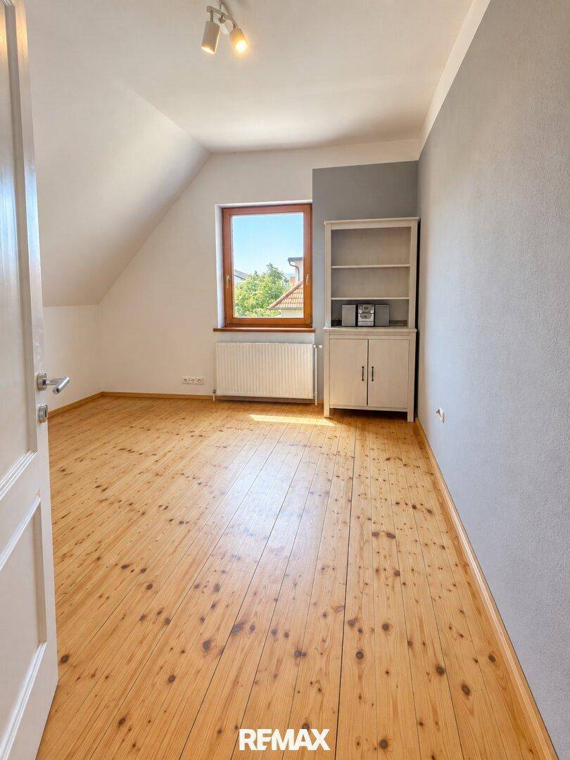 Schlafzimmer mit Holzdielenboden, Dachschräge und einem Fenster mit Blick ins Grüne.