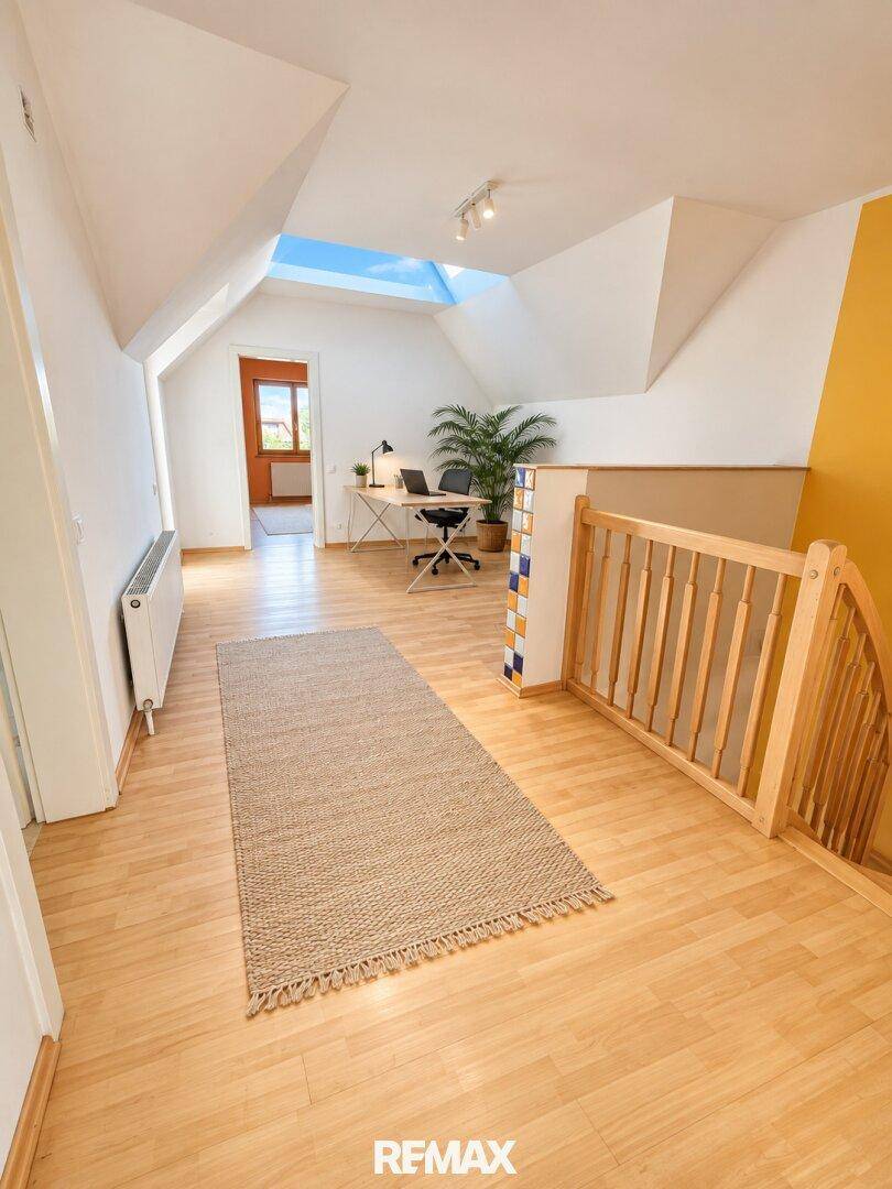 Heller Flur im Dachgeschoss mit Holzboden, Dachfenster und einem kleinen Arbeitsbereich.