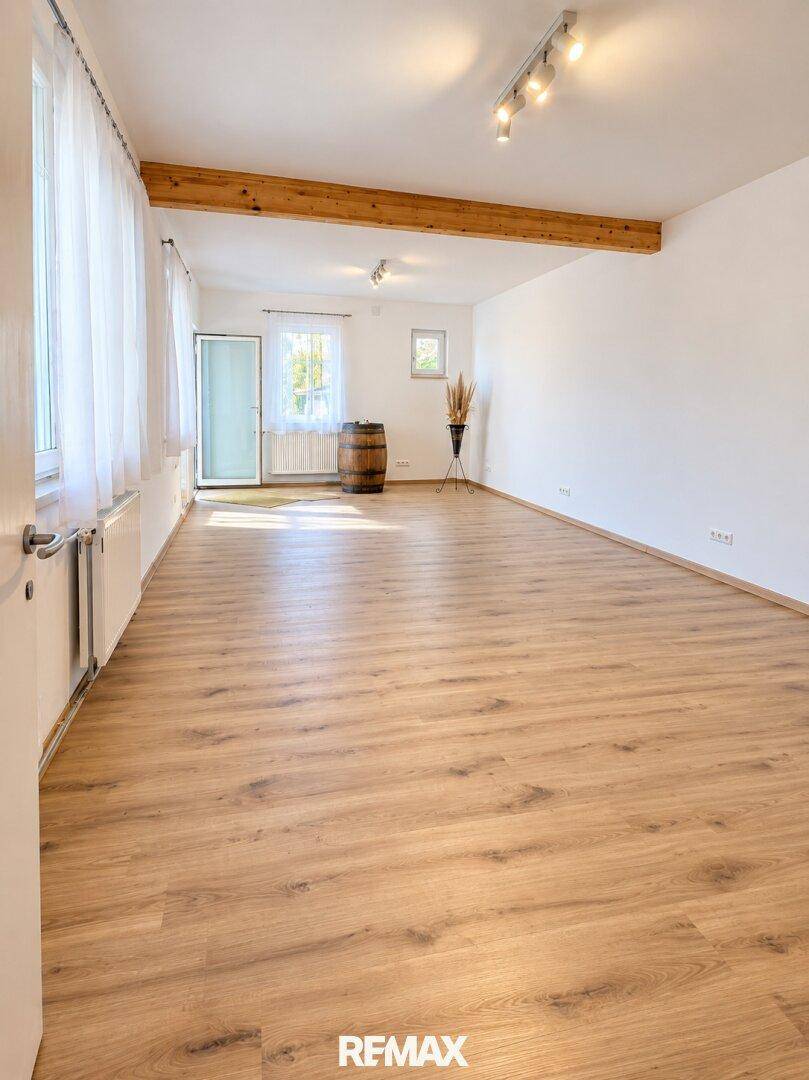 Geräumiger Wohnbereich mit Laminatboden, Holzbalken und Zugang zum Garten durch eine Glastür.