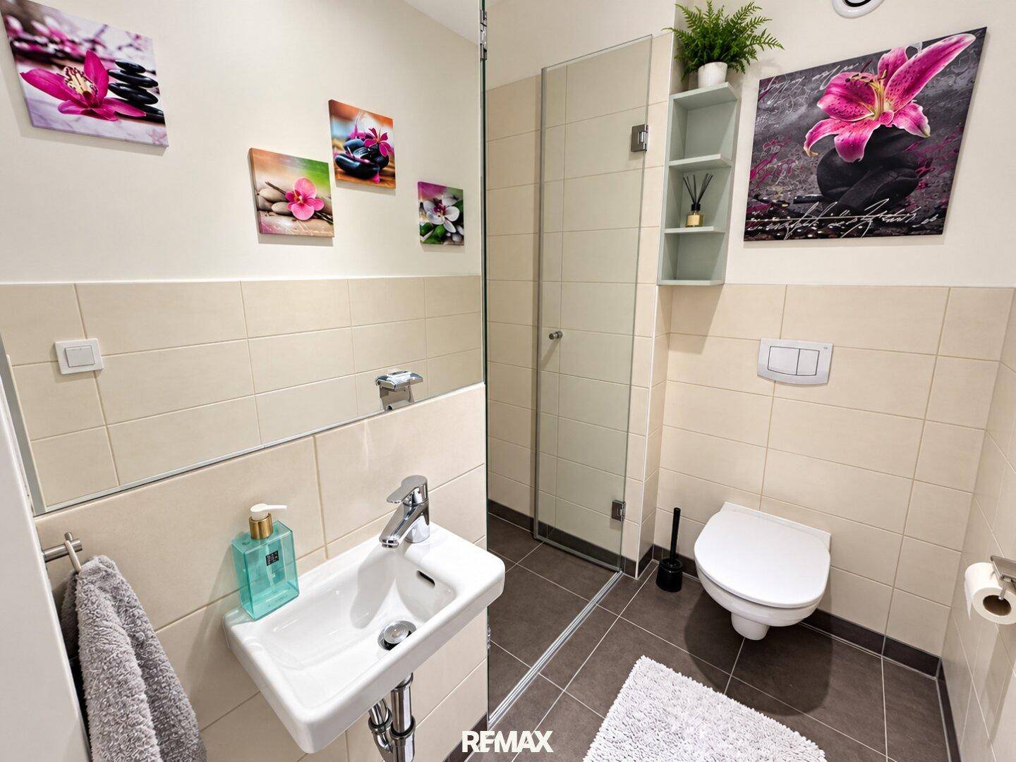 Modernes Gäste-WC mit Dusche, Waschbecken und Wand-WC, hell gefliest.