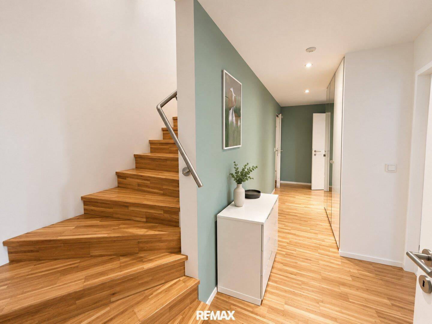 Heller Flur mit Holztreppe und moderner Wandgestaltung, die zu den oberen Etagen führt.