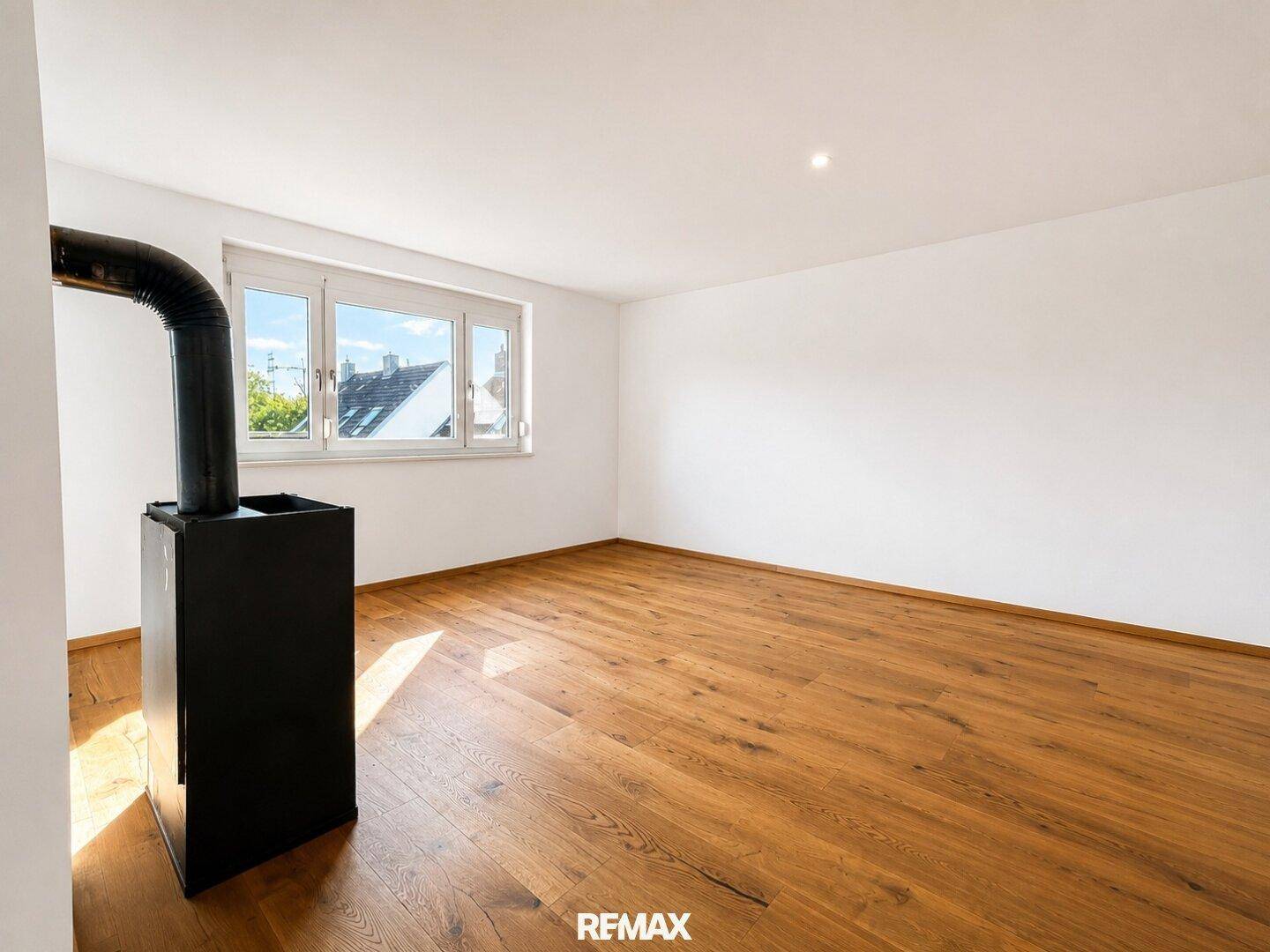 Geräumiger Raum mit Holzboden, weißen Wänden und einem modernen Holzofen für gemütliche Abende.
