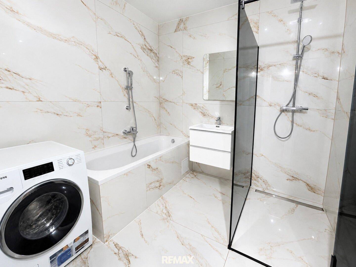 Modernes Badezimmer mit Marmorfliesen, Badewanne, begehbarer Dusche und Waschmaschine.