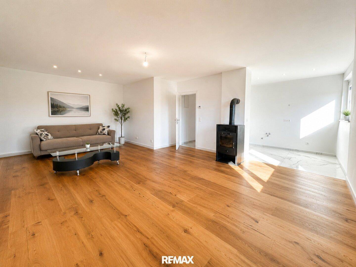 Geräumiger Wohnbereich mit Holzboden, Sofa, Kaminofen und offenem Übergang zu einem gefliesten Bereich.