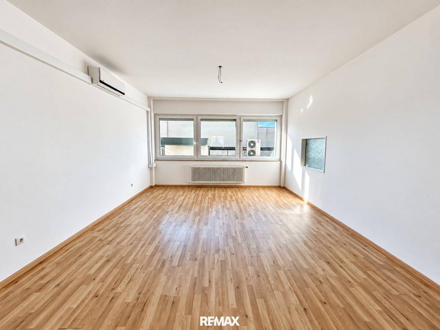 Geräumiges Zimmer mit Parkettboden, Klimaanlage und großen Fenstern für viel Tageslicht.