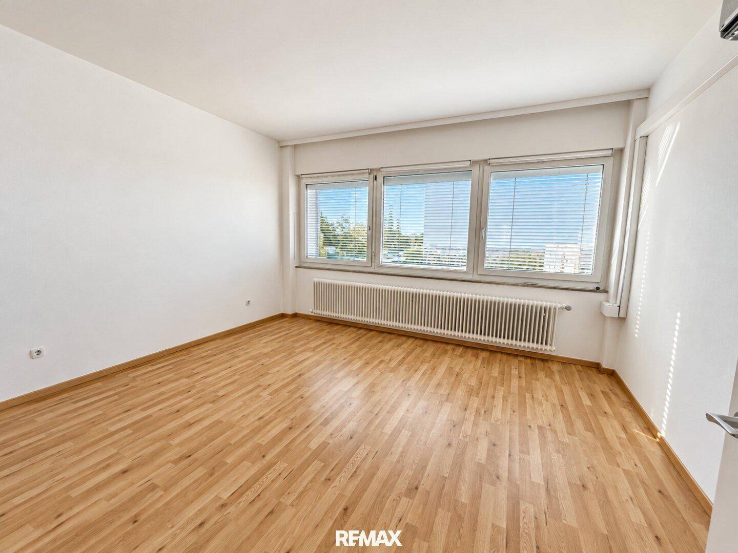 Helles Zimmer mit Parkettboden und großen Fenstern, die einen weiten Blick über die Stadt bieten.
