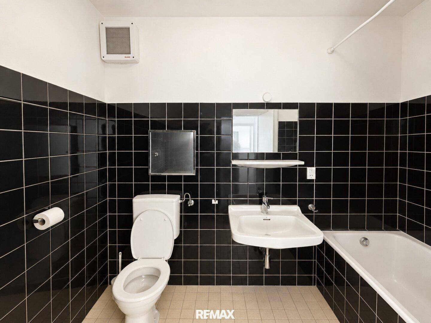 Badezimmer mit markanten schwarzen Fliesen, einer Badewanne und einem WC in gutem Zustand.