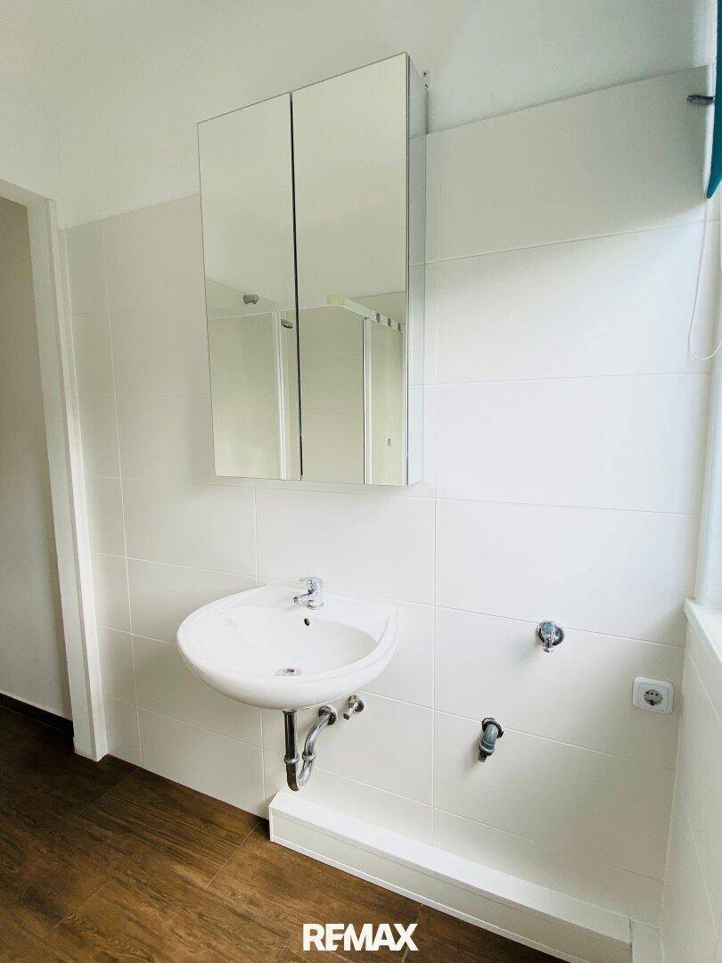 Modernes Badezimmer mit Einzelwaschbecken, Spiegelschrank und weißen Fliesen.
