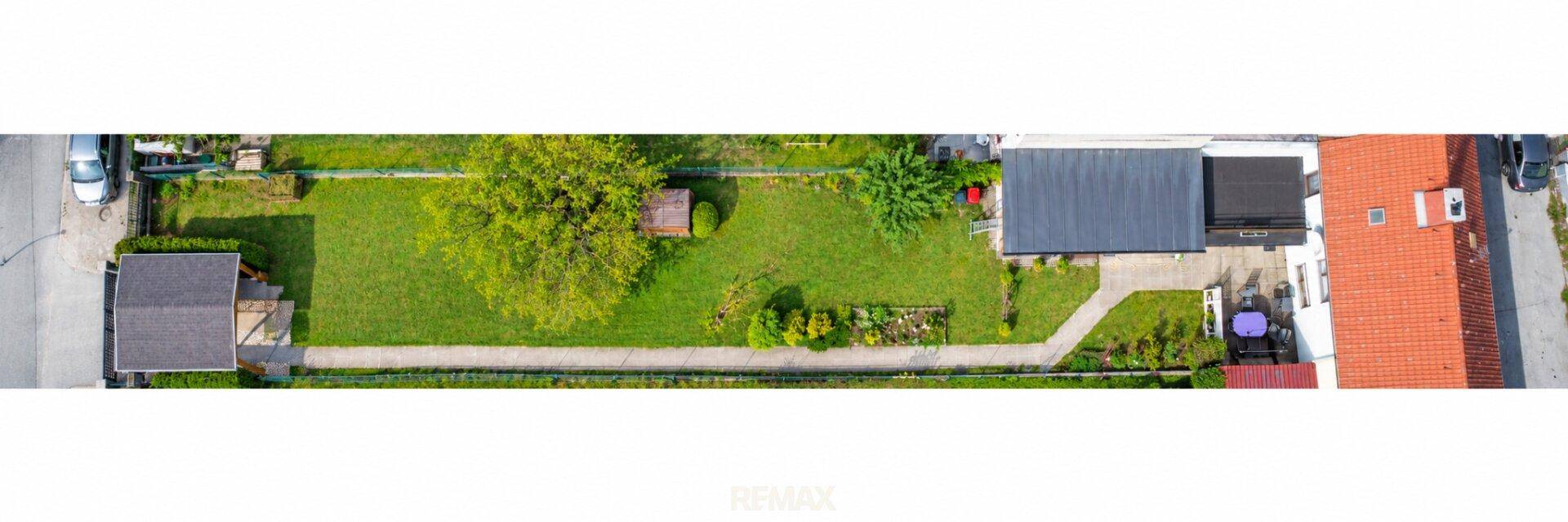 Panorama-Luftaufnahme des Grundstücks mit Haus, langem Garten und Carport.