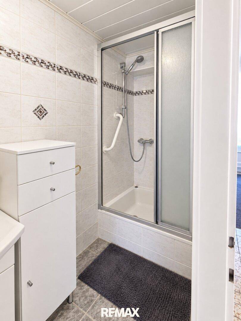 Helles Badezimmer mit Dusch-Badewannen-Kombination, Haltegriffen und weißen Fliesen.