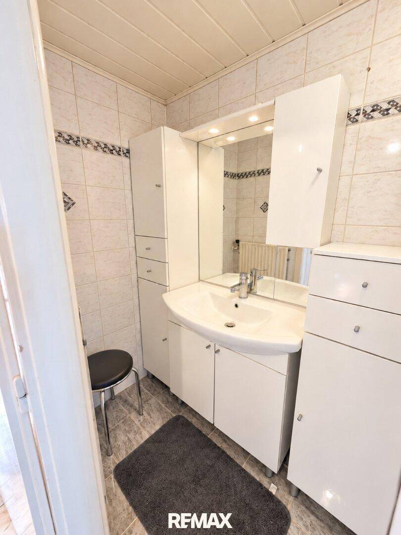 Badezimmer mit Einzelwaschbecken, Spiegelschrank und weißen Badmöbeln.