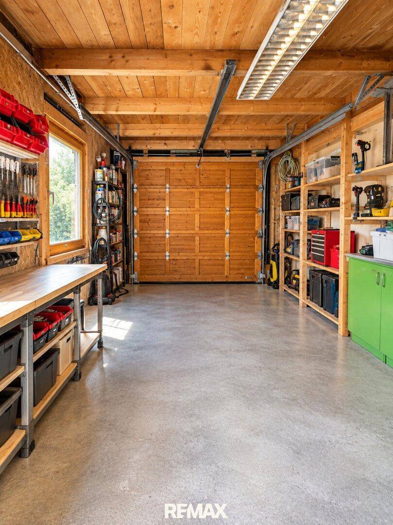 Geräumige Garage mit Werkbank, Regalen und einem großen Holzgaragentor.